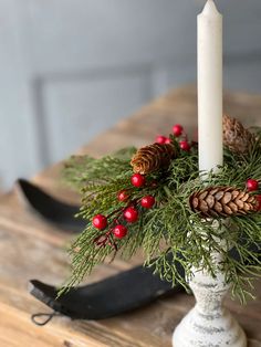 a white candle holder with pine cones and red berries on it, next to a pair of skis