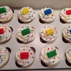 cupcakes with white frosting and lego blocks on them are arranged in a box