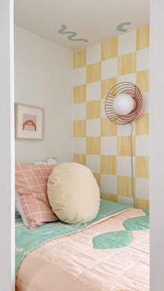 a bedroom with yellow and white checkered wallpaper, pink bedding, and large round pillow