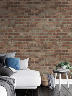 a white couch sitting in front of a brick wall next to a table with a plant on it