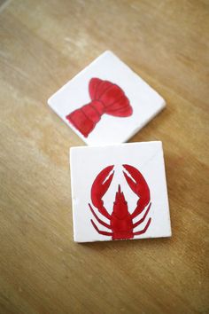 two coasters with red designs on them sitting on a wooden table next to each other