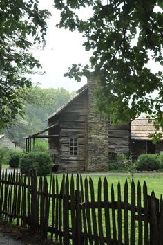 an old log cabin sits behind a wooden fence