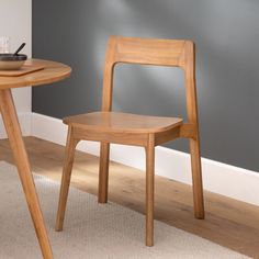 a wooden chair sitting next to a table on top of a carpeted floor in front of a gray wall