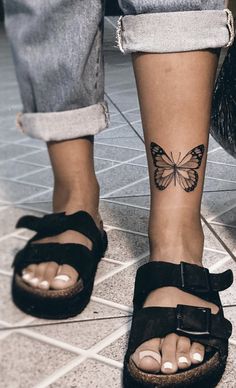 a woman's foot with a butterfly tattoo on her left ankle and black sandals