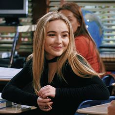 a young woman sitting at a table in front of two other women, one with long blonde hair