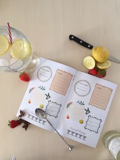 an open recipe book sitting on top of a table next to some lemons and strawberries