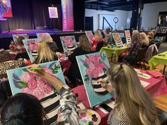 a group of people sitting at tables with paintings on the easels in front of them