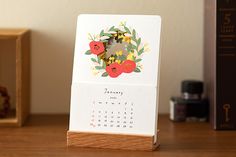 a desk calendar sitting on top of a wooden table next to a small box with an ornament