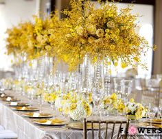 a long table is set with yellow flowers and place settings for the guests to sit down