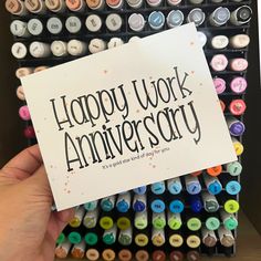 a person holding up a card that says happy work anniversary in front of many colored crayons