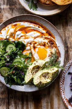 two plates filled with food on top of a wooden table next to bread and salad