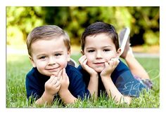 two young boys laying in the grass with their hands under their chins looking at the camera