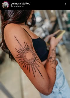 a woman with a sun tattoo on her arm holding a book and looking at the camera