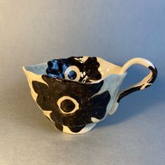 a black and white ceramic cup with eyes on it's side, sitting on a gray surface