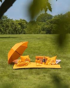 an orange umbrella sitting on top of a yellow blanket in the middle of a field