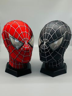 two spider - man masks are sitting side by side on black bases, one is red and the other is black