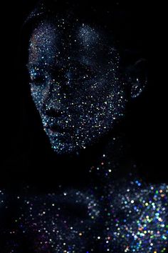 a woman with glitter on her body in the dark, she is looking down at something