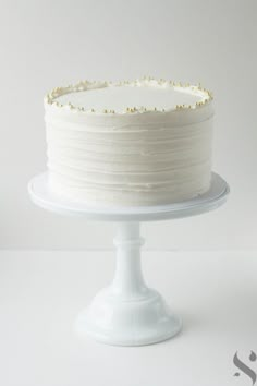 a white cake with gold sprinkles sitting on top of a pedestal plate