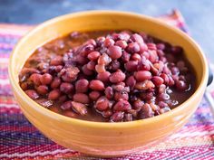 a yellow bowl filled with beans on top of a checkered table cloth next to a spoon