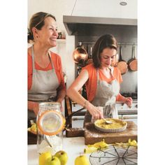 two women in aprons are preparing food on a counter top with lemons and apples