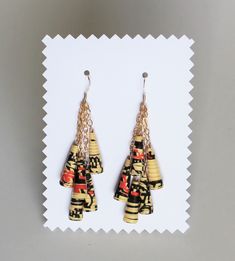 two pairs of earrings are shown on a white cardigane paper with black, yellow and red designs