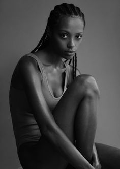 a black and white photo of a woman with braids sitting on the floor wearing a tank top