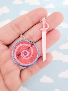 a hand holding a pink and blue keychain with an object in the middle