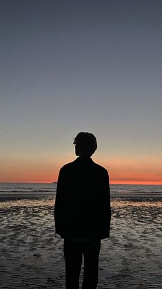 a man standing on top of a sandy beach next to the ocean at sunset or dawn