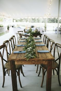 a long wooden table set with place settings and greenery on the tables for an outdoor wedding reception