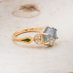 a gold ring with a blue and green stone surrounded by diamonds on a wooden surface