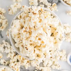 a white bowl filled with popcorn on top of a marble counter next to other bowls