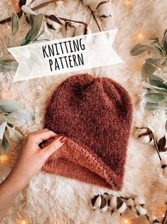 someone is knitting a knitted hat on top of a white rug with greenery