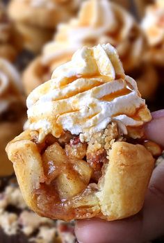 a hand holding up a pastry with whipped cream on top and other pastries in the background