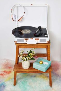 a record player sitting on top of a wooden table next to a vase with flowers