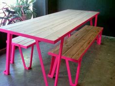 a pink table with two benches next to it on the floor in front of a potted plant