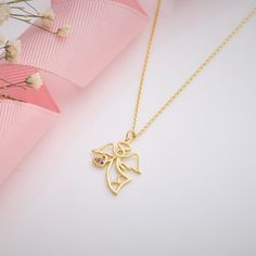 a gold necklace with an angel charm on it and flowers in front of the necklace