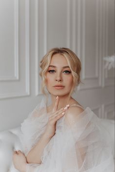 a woman sitting on top of a white couch wearing a dress and posing for the camera