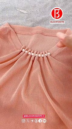 someone is stitching on the back of a pink shirt with white buttons and beads