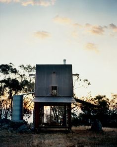 a small house sitting on top of a dry grass field next to a blue barrel