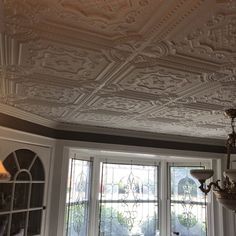 an ornate ceiling in the corner of a room with two windows and a chandelier