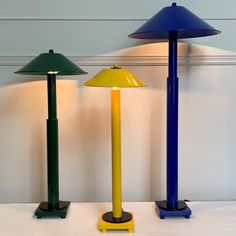 three different colored lamps sitting next to each other on a white counter top in front of a wall