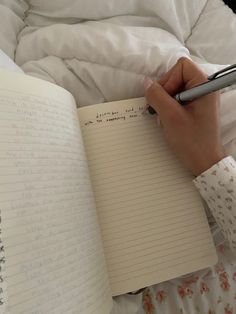 a person writing in a notebook with a pen on top of the page and an open book next to it