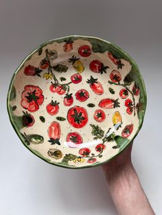 a hand holding a bowl with tomatoes painted on the bottom and green trim around it