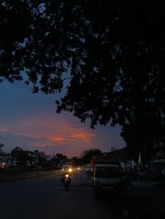 the sun is setting over a street with parked cars