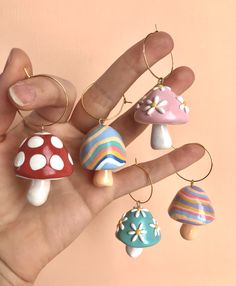 a hand holding several different colored mushrooms on it's fingers and wearing gold hoop earrings