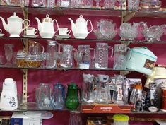 a shelf filled with lots of glassware on top of wooden shelves in front of a pink wall