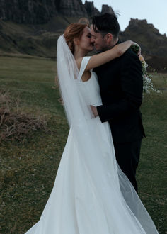 a bride and groom embracing each other in front of a mountain range at their wedding