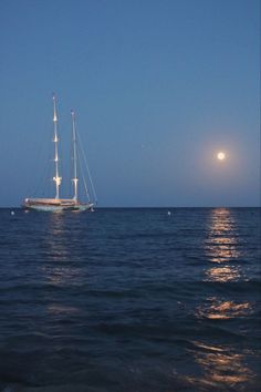 a sailboat in the ocean at night with full moon behind it and blue sky