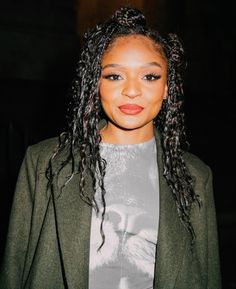 a woman with long curly hair wearing a green blazer and grey t - shirt