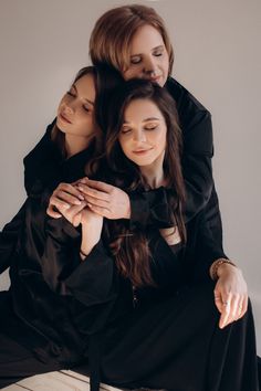 three women sitting on top of each other in black dresses and one is holding her arms around the other